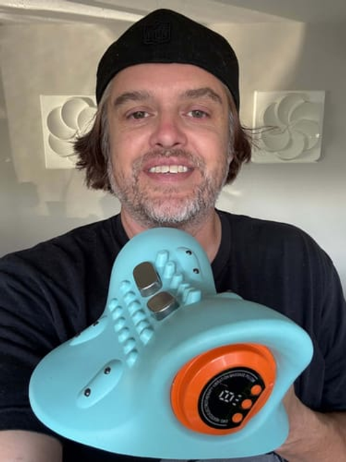 Man holding the turquoise massager with its orange side dial visible