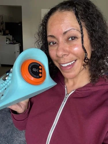 Woman in a burgundy top holding the massager beside her face