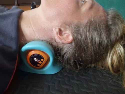 Woman resting her neck on the massager on a dark mat